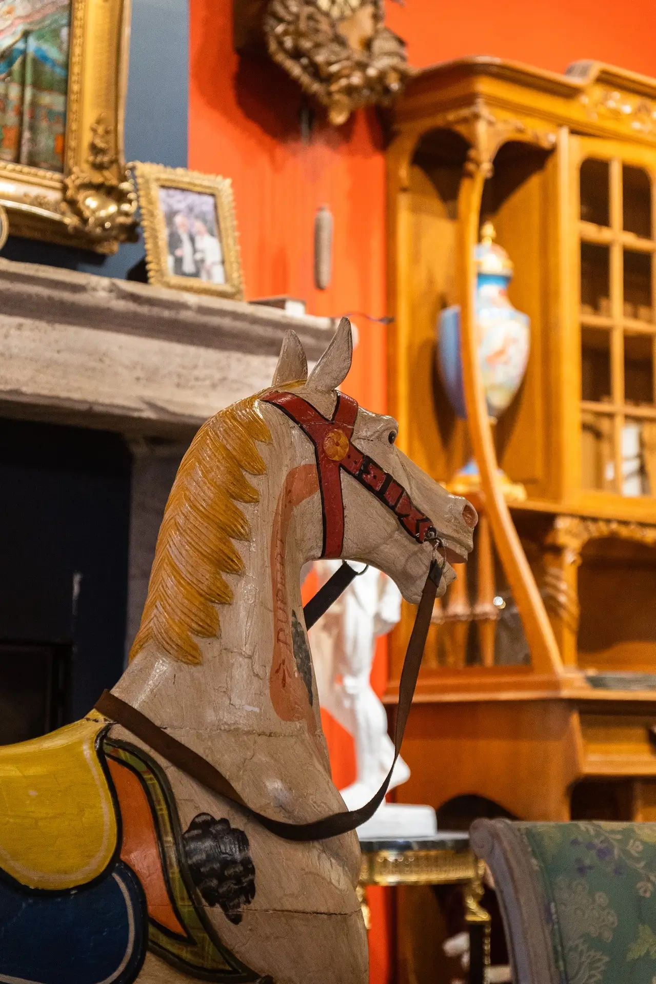 Cheval en bois peint exposé dans une pièce décorée avec des antiquités et meubles anciens.